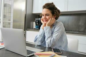 imagen de sonriente mujer estudiando en remoto, mirando a ordenador portátil mientras sentado a hogar, acecho seminario web, haciendo en línea curso en computadora foto