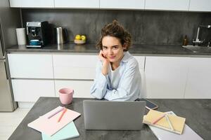 Image of young working woman, looking at laptop, sitting at home and watching webinar, connecting to team meeting, studying indoors photo
