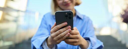 cerca arriba retrato de teléfono inteligente en manos de joven mujer, quien se sienta y descansa en escalera al aire libre foto