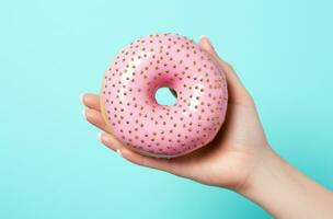 AI generated pink doughnut held by a hand against a blue background photo