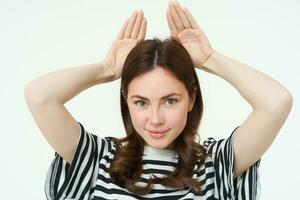 Image of cute brunette girl shows animal eats with hands on top of head, smiling and looking happy, white background photo