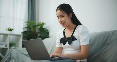 Portrait of Young asian woman relaxing at home sit on comfortable couch using laptop, chatting with friends in social network, do remote job, shopping online photo