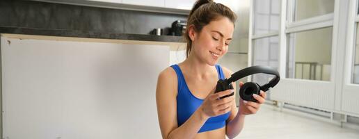 Portrait of woman in tracksuit, doing yoga training, workout at home with wireless headphones, listening music to focus photo