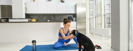 Portrait of smiling, beautiful woman doing sports, workout from home with her black dog, doing sports in living room photo