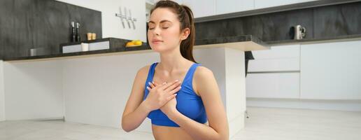 Woman practicing yoga and meditation at home sitting in lotus pose on yoga mat, relaxed with closed eyes. Mindful meditation concept. Wellbeing photo