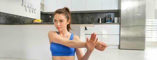 Image of fitness girl concentrates on workout, stretches hands before training session at home, follows online gym instructions photo