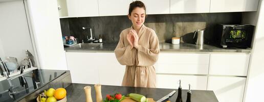 Portrait of woman in kitchen getting creative, thinking what to cook with vegetables, preparing healthy food, making dinner, looking at chopping board with zucchini and peppers photo