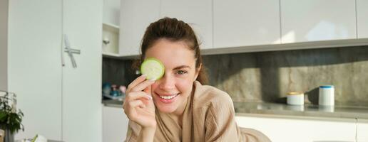 Close up portrait of happy, beautiful girl, chopping zucchini, smiling, posing in the kitchen while making food, preparing salad for lunch, eating healthy photo