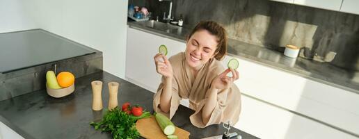 Portrait of beautiful brunette woman in the kitchen, wearing bathrobe, chopping vegetables on board, cooking healthy vegetarian food, preparing salad, making a meal photo