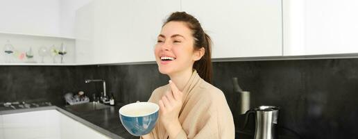 Portrait of good-looking young woman starting her day with cup of coffee, standing in the kitchen and drinking cappuccino from big mug, enjoying favourite drink in the morning photo