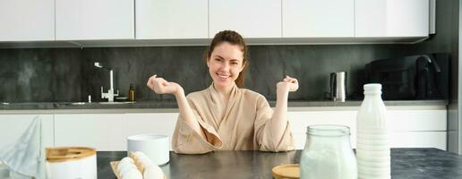 Attractive young cheerful girl baking at the kitchen, making dough, holding recipe book, having ideas photo