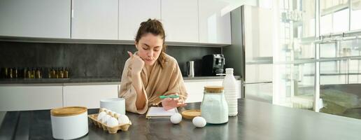 atractivo joven alegre niña horneando a el cocina, haciendo masa, participación receta libro, teniendo ideas foto