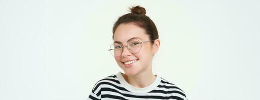 imagen de joven mujer en anteojos, utilizando su móvil teléfono, en pie con teléfono inteligente y sonriente, en pie terminado blanco antecedentes foto