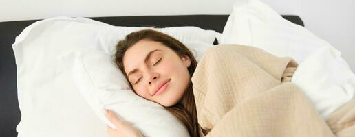 Portrait of smiling brunette woman in pyjamas, sleeping in hotel bed, relaxing with pleased face, dreaming, sleeping in bedroom photo