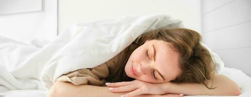 retrato de contento joven mujer dormido en su cama, disfrutando un siesta en hotel suite, acostado debajo cobija foto