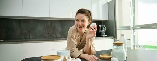 Attractive young cheerful girl baking at the kitchen, making dough, holding recipe book, having ideas photo