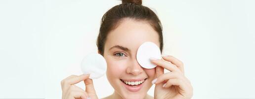 Beauty and female concept. Close up portrait, young woman holding cotton cosmetic pads near her face and smiling, removes makeup, uses daily facial cleanser, stands over white background photo