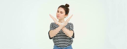 Portrait of confident young woman, showing cross sign, prohibit gesture, disapprove something, isolated against white background photo