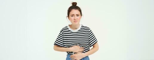 Woman feeling hungry, touching her belly. Girl with period cramps, menstrial pain, holds hands on stomach that aches, isolated over white background photo