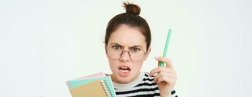 Close up portrait of woman shouting, wearing glasses, shaking pen and holding paperwork, notebooks, teacher arguing, scolding someone, standing over white background photo