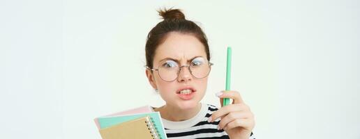 Portrait of angry woman in glasses, teacher scolding someone, shaking pen and arguing, holding notebooks, standing over white background photo