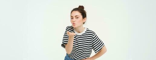 Portrait of cute young woman blows air kiss, sends mwah at camera, posing cute against white background. Lifestyle and people concept photo