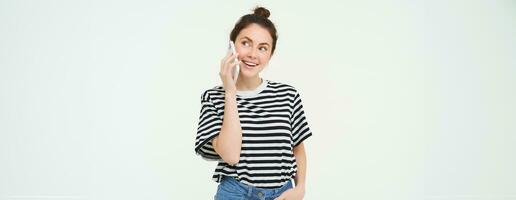 Happy young woman talks on mobile phone, chats on telephone, uses smartphone, stands over white background photo