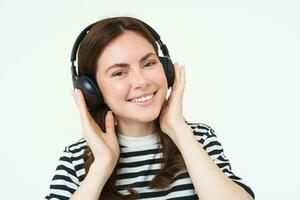 retrato de hermosa mujer en inalámbrico auriculares, escuchando música, utilizando auriculares, sonriente a cámara, en pie terminado blanco antecedentes foto