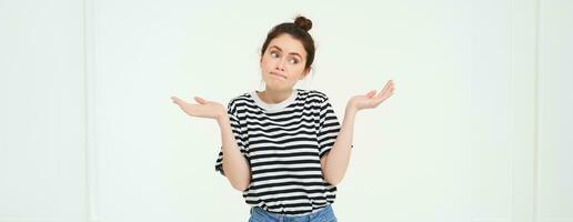 Image of confused brunette girl shrugging shoulders, looks puzzled, isolated over white background photo