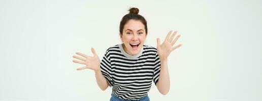 Portrait of happy, beautiful girl makes jazz hands, tells big news, revelation, introduces surprise, stands over white background photo