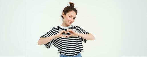 Beautiful european woman, shows heart sign, expresses her love and affection, flirting, standing over white background photo