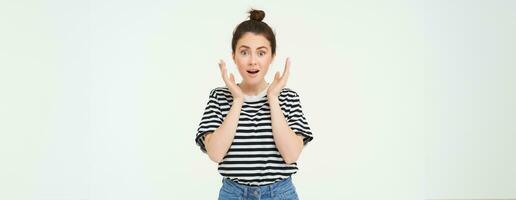 Portrait of surprised woman gasping, looking amazed, hear great news, drops jaw, says wow, impressed by something, stands over white background photo