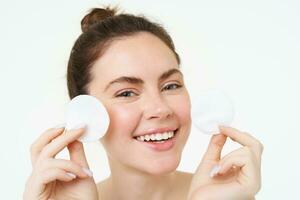 Beauty woman with clear glowing face, showing cotton cosmetic pads for makeup removal, cleansing her facial skin, standing over white background photo