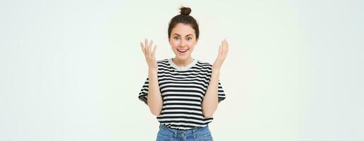 Image of excited girl clap hands, applause, looks surprised and happy, celebrates due to great news, stands over white background photo