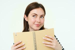 Portrait of young woman makes notes in her planner, writes in diary, checks her schedule in notebook, holding organizer in hands, stands over white background photo