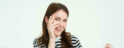 Portrait of attractive, smiling young woman, laughing and smiling, touches her face, standing over white background photo