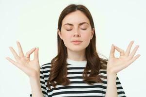 Everything under control. Young woman meditating, standing in zen, yoga pose, keeps calm, posing with closed eyes, breathing with relaxed mindful expression photo