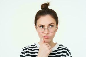 Image of woman in glasses, thinking, pondering smth, looking away with thoughtful face, analizing, standing over white background photo