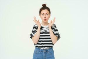 Lifestyle and emotions concept. Portrait of girl with surprised face expression, saying wow, looks impressed at camera, stands over white background photo