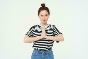 Image of young woman shows namaste gesture, holds hands together, says thank you, expresses gratitude, stands over white background photo