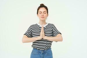 Portrait of young mindful woman meditating, holds hands clasped together, namaste gesture, practice yoga, standing over white background photo