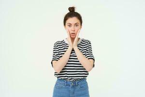 Lifestyle and emotions concept. Portrait of girl with surprised face expression, saying wow, looks impressed at camera, stands over white background photo