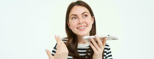 Portrait of happy young woman, student recording voice message, holding smartphone near lips, talking into mobile phone speakerphone, explaining something, singing, translating her words photo