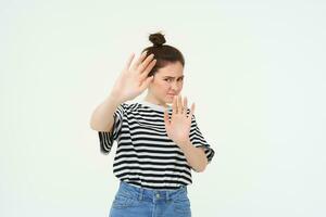 Image of woman refusing something, raising hands in defensive gesture, protecting herself, rejecting offer, declining, standing over white background photo