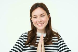 Portrait of young woman expresses her gratitude, shows thank you, namaste gesture, holding hands clasped together near chest and smiling, standing over white background photo