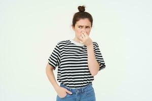 joven mujer cierra su nariz con dedos desde asqueroso oler, aislado en blanco antecedentes foto