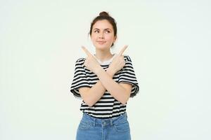 Portrait of beautiful, smiling young woman standing puzzled, makes choice, decides what to pick, points sideways left and right, stands over white background photo