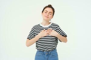 Passionate girl holds hands on her heart and smiles, stands over white background photo