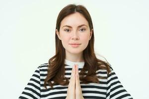 retrato de joven mujer expresa su gratitud, muestra gracias tú, namaste gesto, participación manos abrochado juntos cerca cofre y sonriente, en pie terminado blanco antecedentes foto