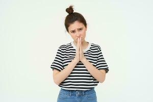 Please. Young woman asks for help, begs you, holds hands in pray, pleading, isolated against white background photo